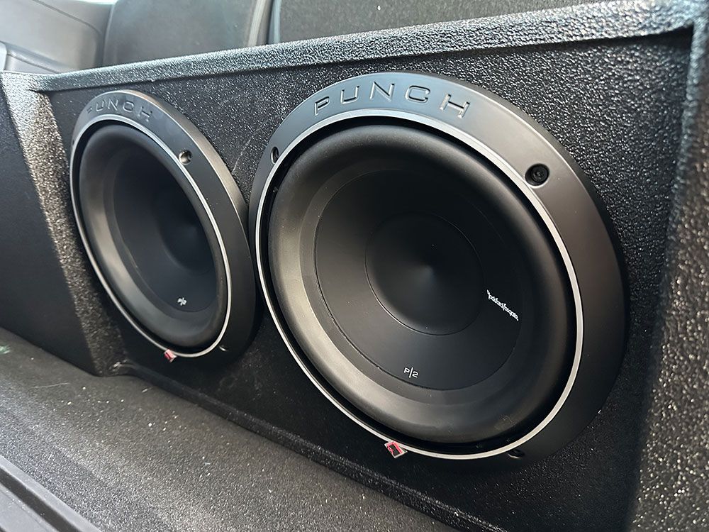 Two Rockford Fosgate Punch subwoofers in a black speaker box, likely in a car.