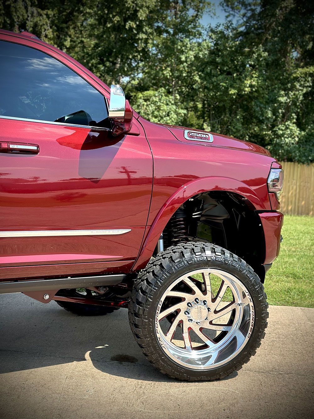 Red lifted pickup truck with chrome rims parked on a driveway, with tinted windows and a blurred background.