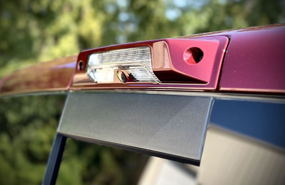 Red truck's rear, with a backup camera lens, brake light, and black tailgate protector.