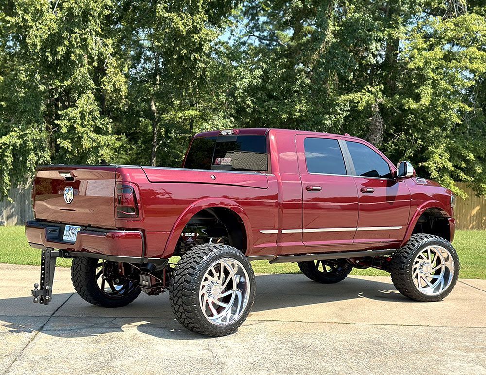 Red lifted pickup truck with chrome wheels and a black tow hitch parked outside.