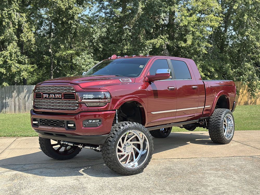 Red lifted Dodge Ram truck with chrome wheels parked on pavement.