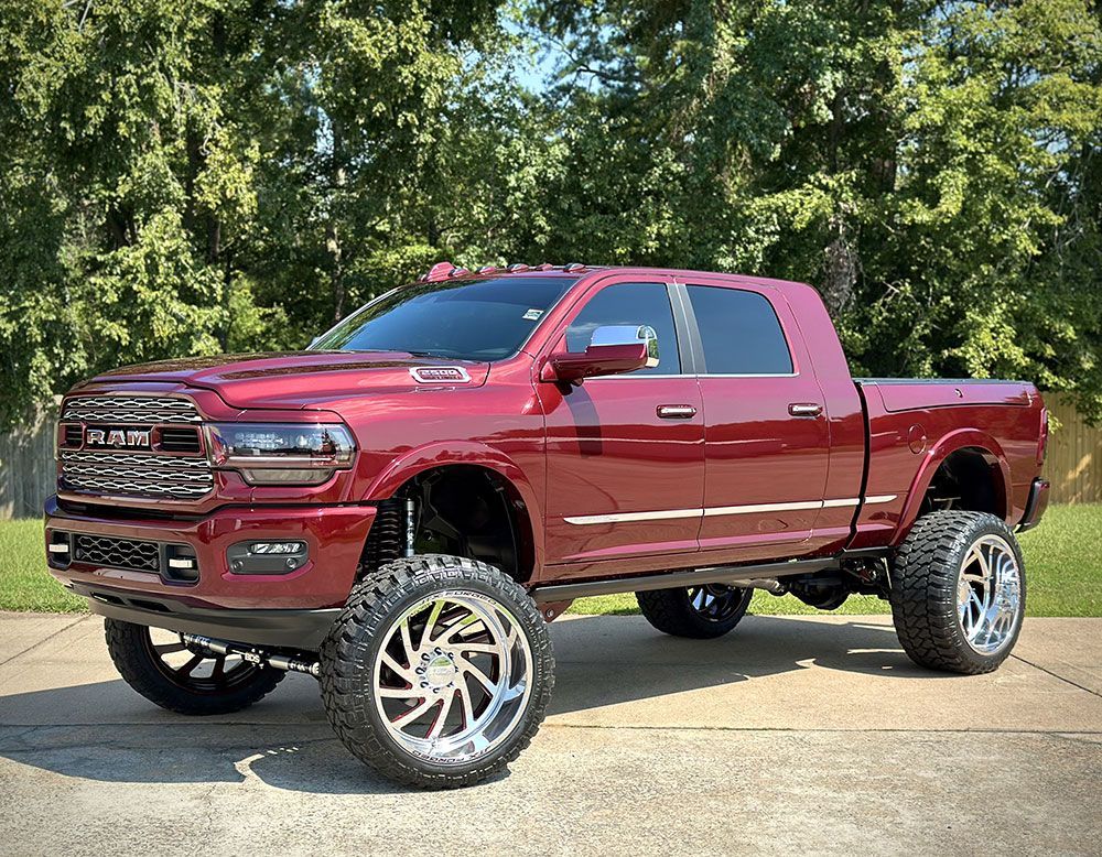 Red lifted RAM truck with chrome wheels parked outdoors.