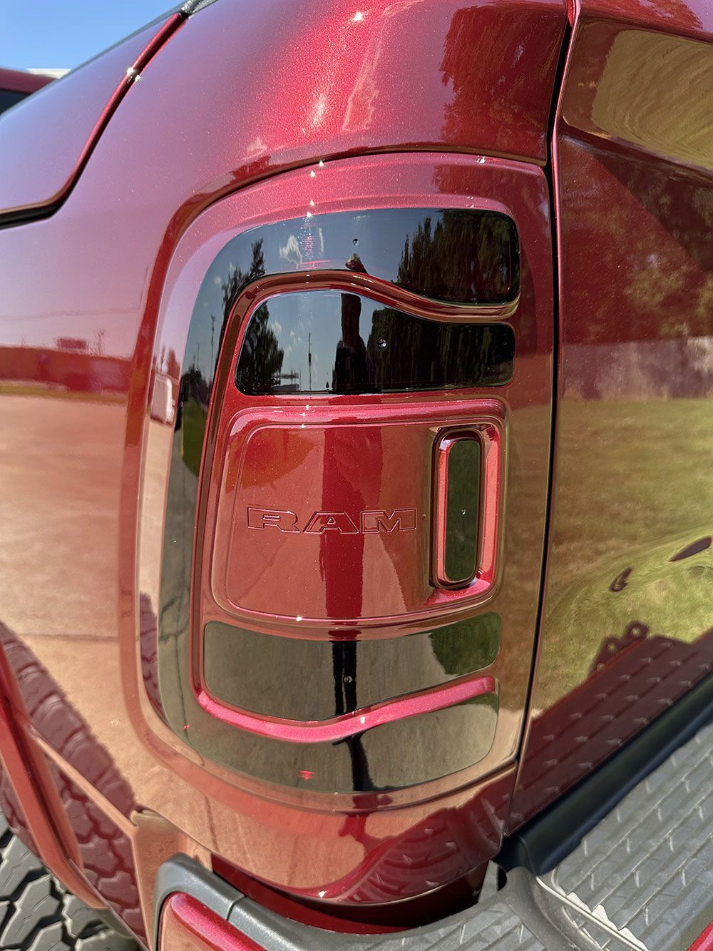 Close-up of a maroon-colored truck's tail light with black accents, reflecting sunlight.