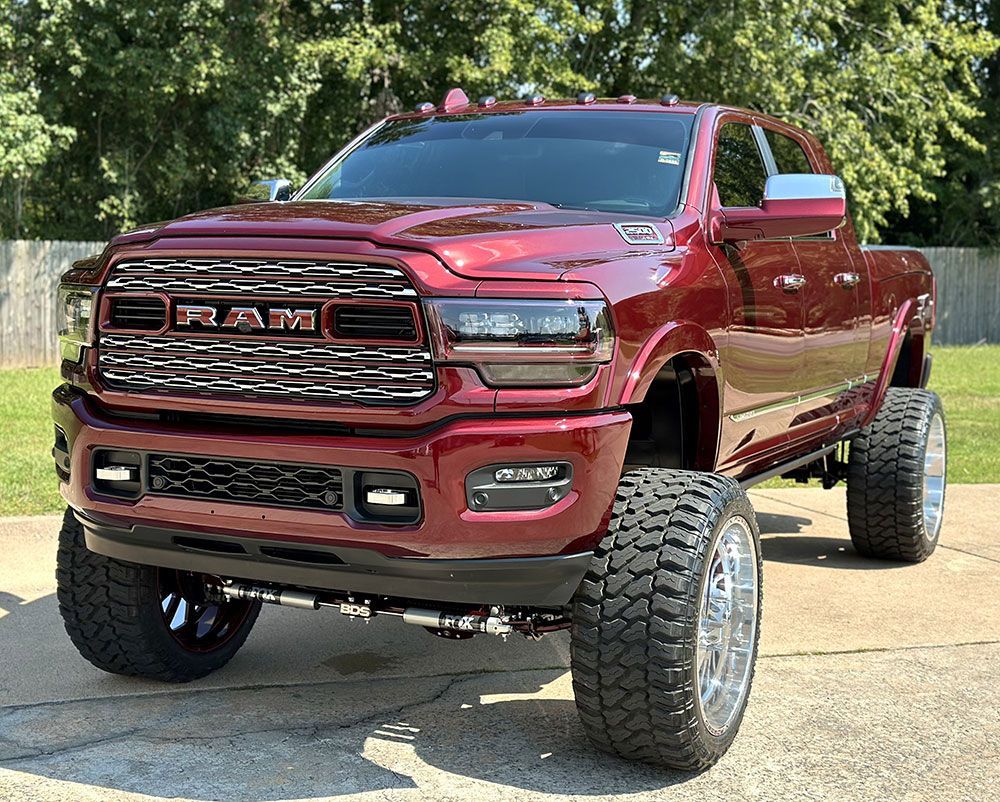 Red Ram pickup truck with large chrome wheels, lifted suspension, and a black front bumper.