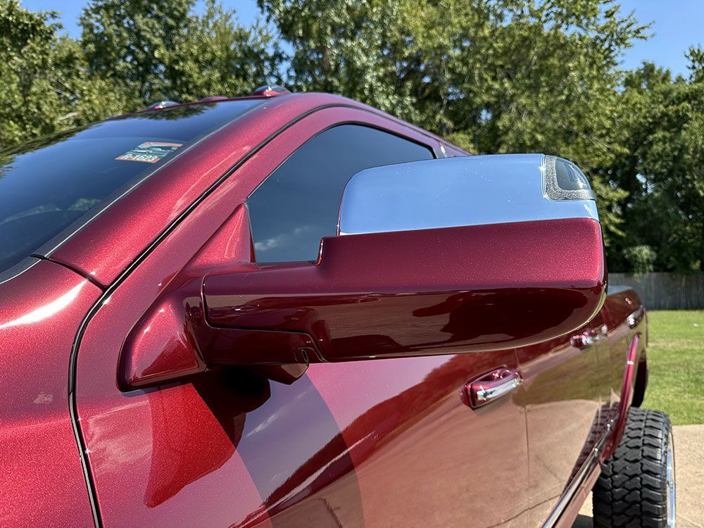 Red pickup truck with chrome side mirror, parked on grass.