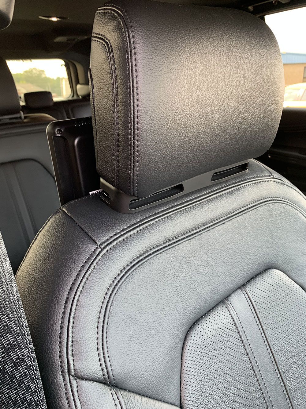 Black leather car seat headrest with stitched detailing, and a media device mount.