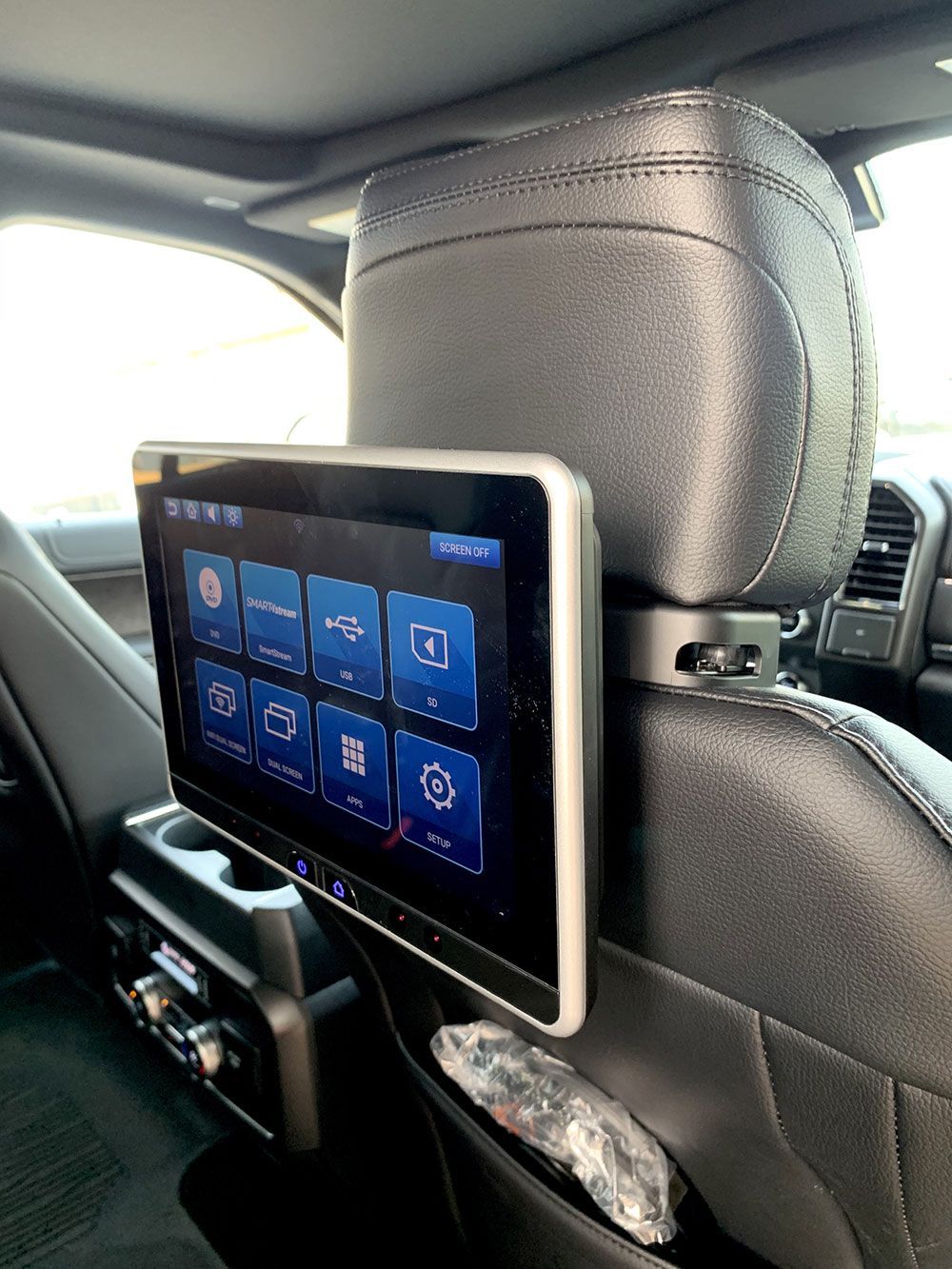 Rear car seat with a mounted entertainment screen displaying a user interface with blue icons.