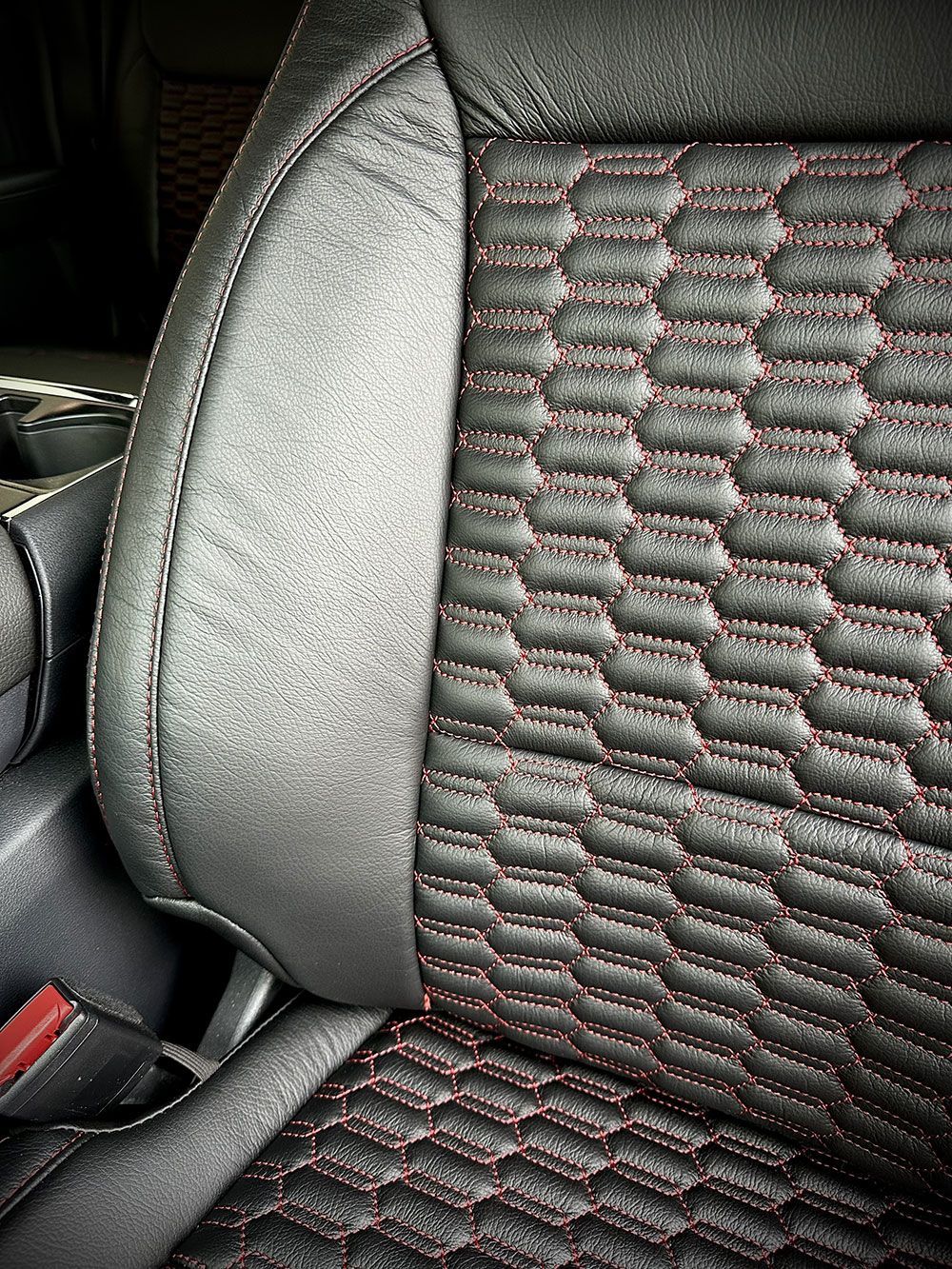 Black car seat with red stitching in a honeycomb pattern.