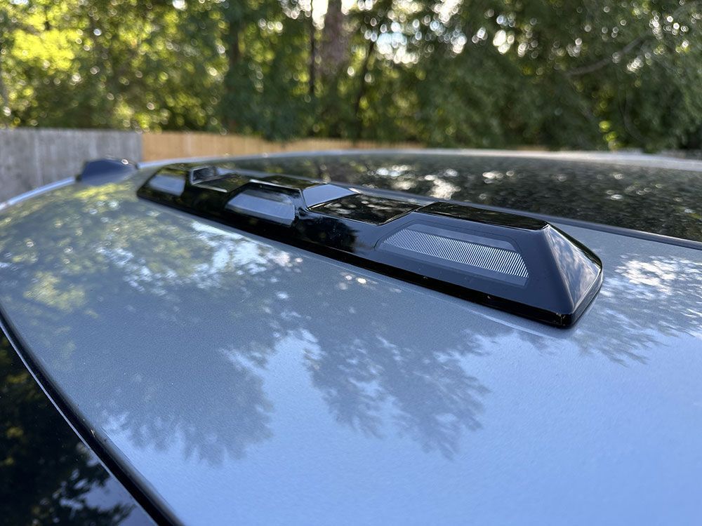 Black roof spoiler on a silver car roof, outdoors with trees in the background.