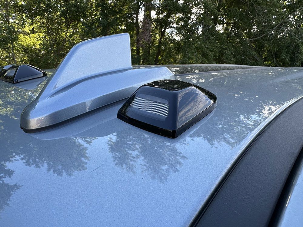 Silver car roof with a shark fin antenna and a black square vent.