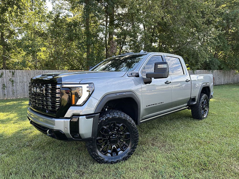 Gray GMC Denali truck parked on grass, with black wheels and a black grille, outdoors.