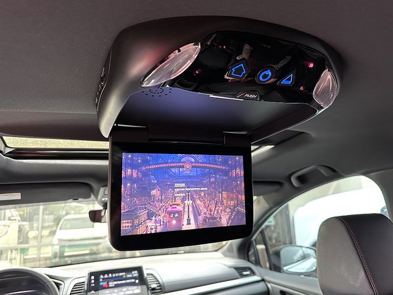 Car interior with a built-in entertainment screen displaying a video; overhead console with lights and controls.
