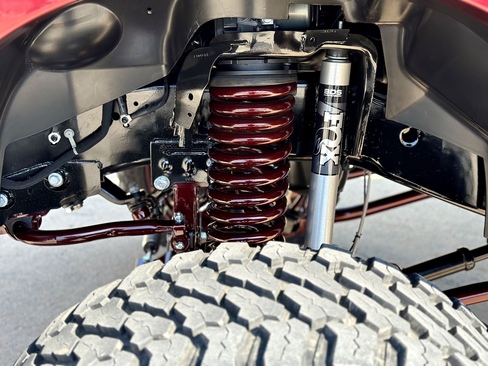 Close-up of a truck's suspension with a red coil spring, black frame, and a Fox shock absorber.