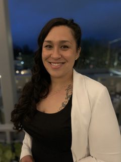A woman wearing a white jacket and a black shirt is smiling for the camera.