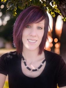 A woman with purple hair is wearing a black shirt and a black necklace