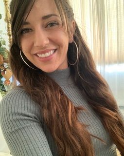 A woman wearing a grey sweater and hoop earrings is smiling for the camera.