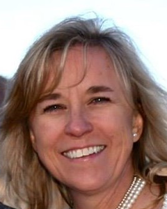 A close up of a woman wearing a pearl necklace and smiling.