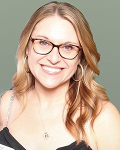 A woman wearing glasses and hoop earrings is smiling for the camera.