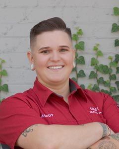 A woman in a red shirt is smiling with her arms crossed.