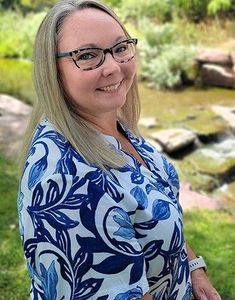 A woman wearing glasses and a blue and white floral shirt is smiling for the camera.