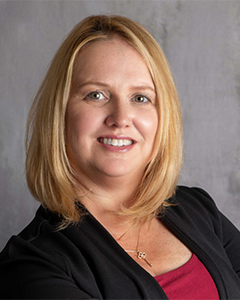 A woman wearing a black jacket and a red shirt smiles for the camera