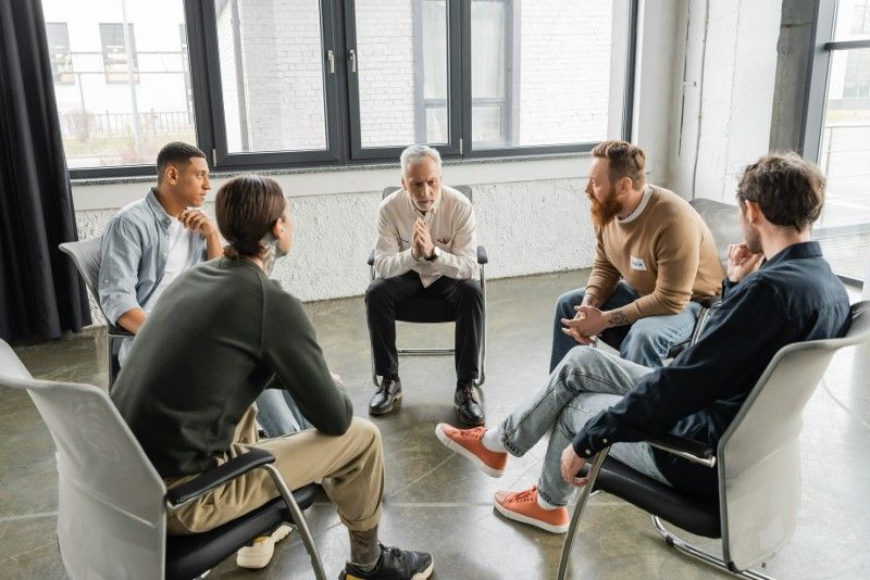 A group of men are sitting in chairs in a circle having a conversation.