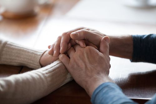 Two people holding hands across a table in a close-up, supportive gesture