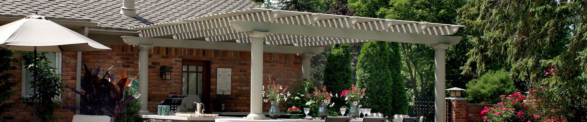 A brick house with a pergola and umbrellas in front of it.