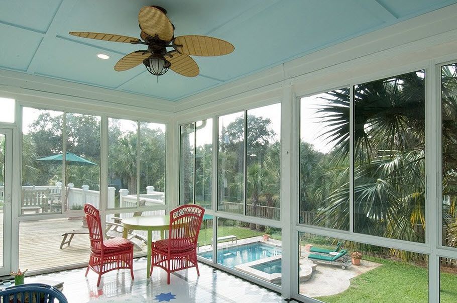 A screened in porch with a table and chairs and a ceiling fan