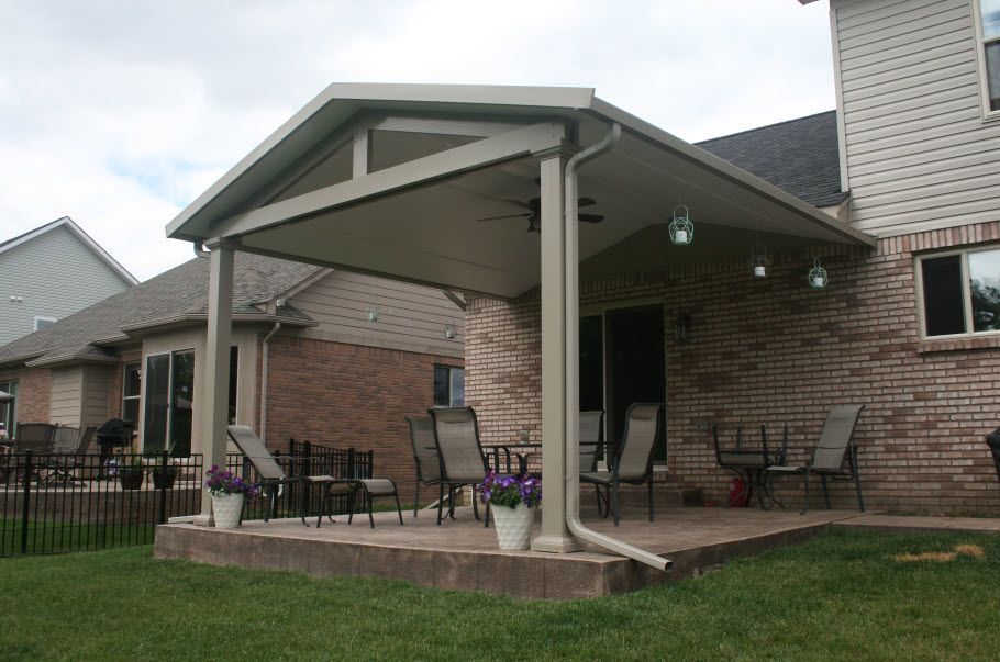A covered patio with chairs and tables in front of a brick house.