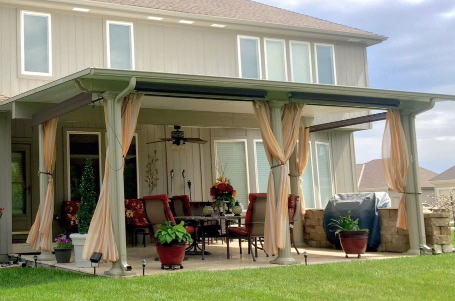 A large house with a covered patio with tables and chairs and curtains.