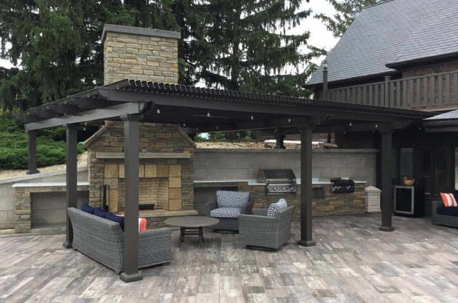 A patio with a couch , chairs , table and fireplace under a pergola.