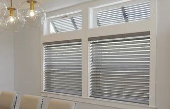 Windows with gray blinds in a white-walled room, with upper windows tilted open.
