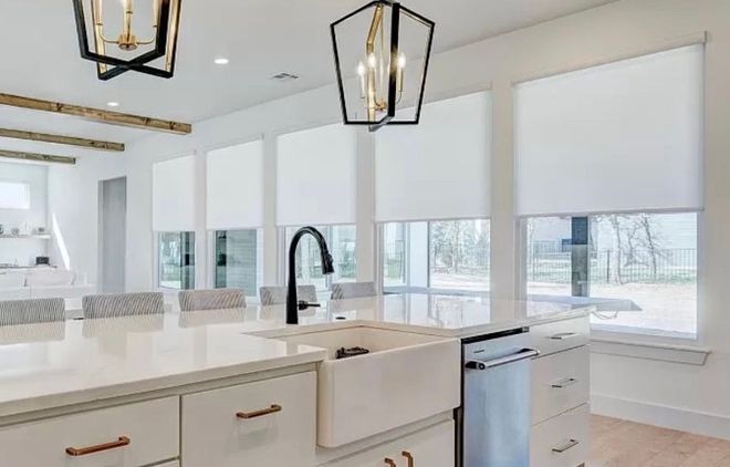 Modern kitchen with white cabinetry, island, black faucet, and white roller shades.