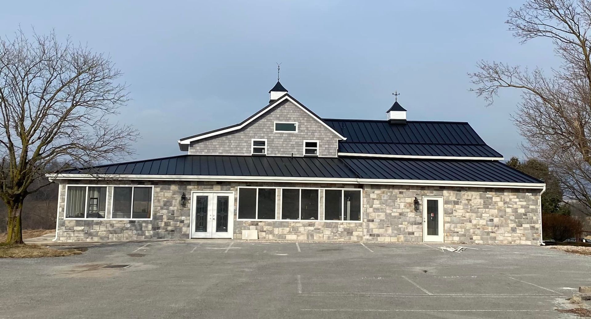 Stone building with black roof and multiple windows, in a rural setting with bare trees.