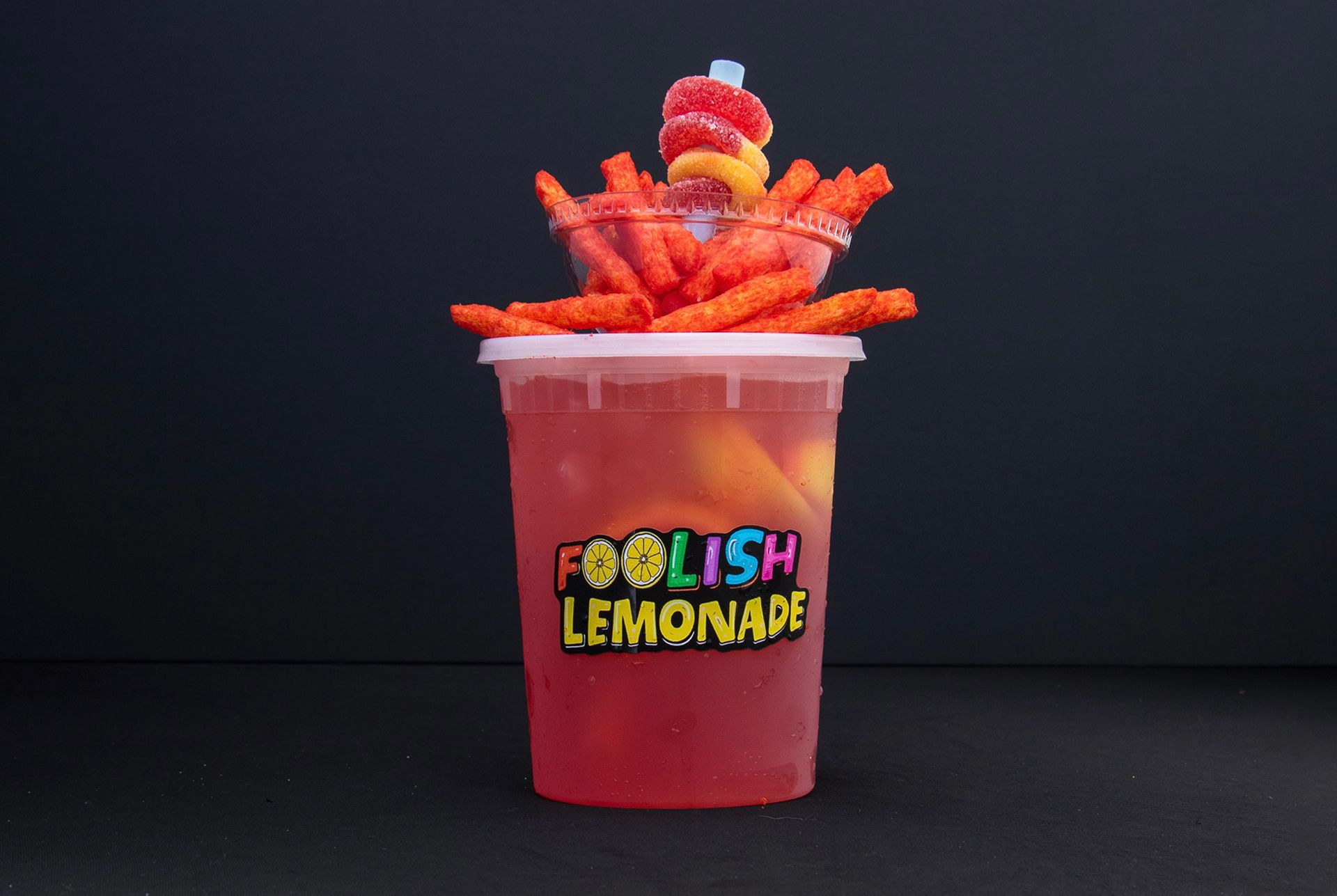 Clear cup of red drink topped with fries and gummy candy.