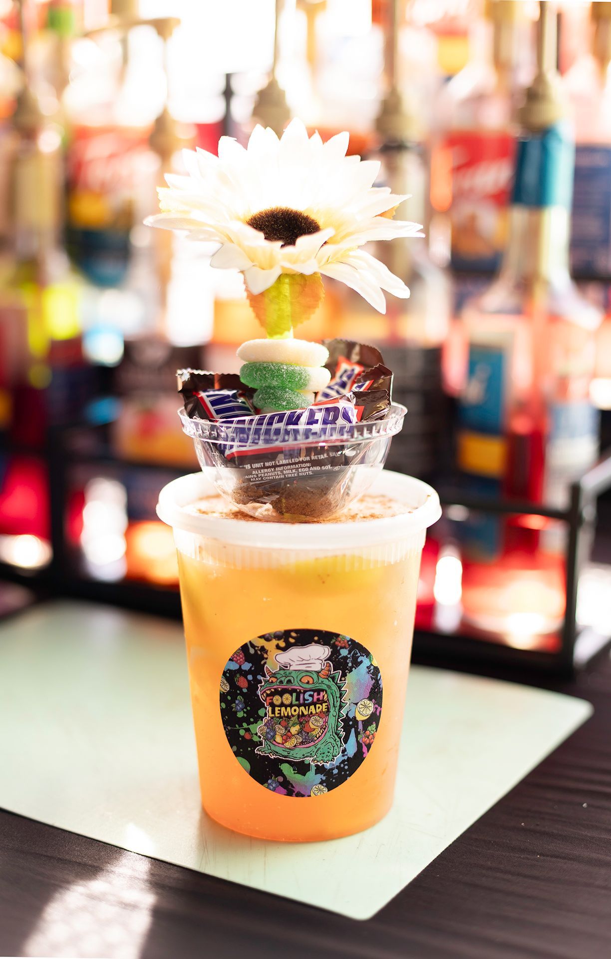 Tropical cocktail in a clear cup, topped with a flower, on a table with a blurred bar background