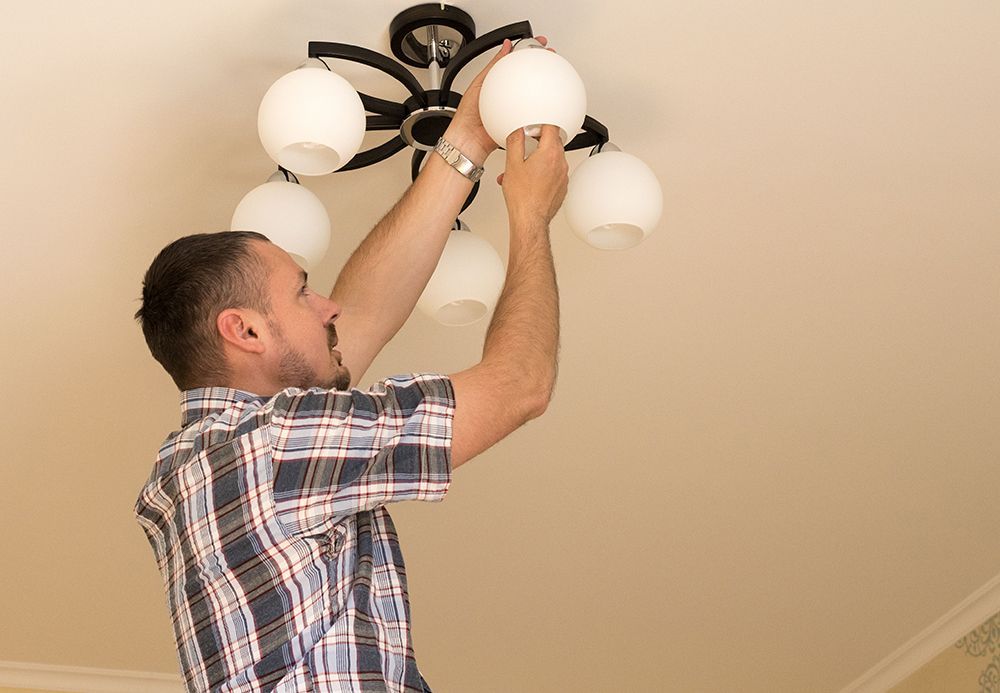 Man installing a ceiling light fixture on a beige ceiling