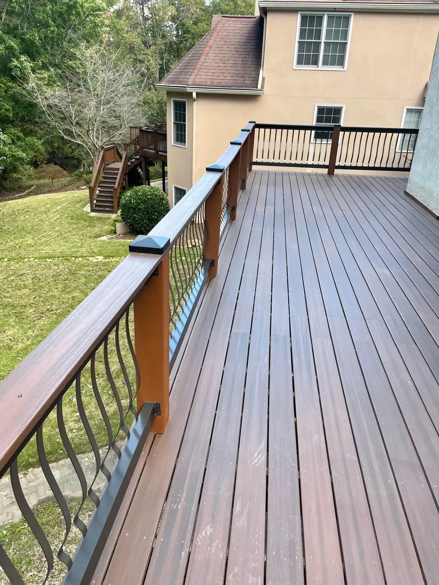 Wooden deck with brown and black railing overlooking a yard and house.