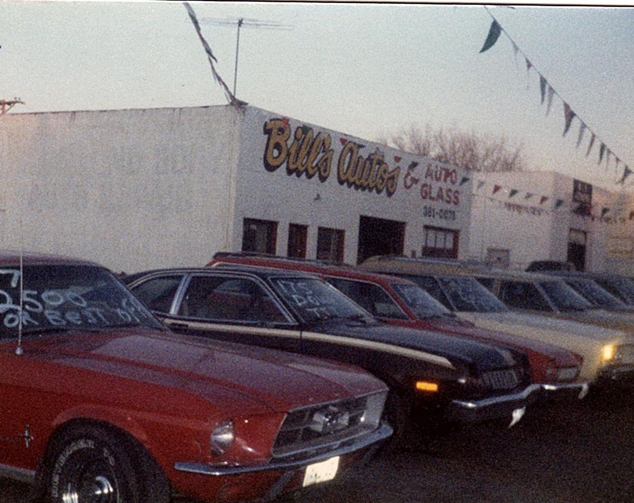 A row of cars are parked in front of Bill's Auto Glass building
