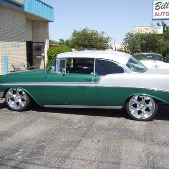 A green and white car is parked in front of a bill auto store
