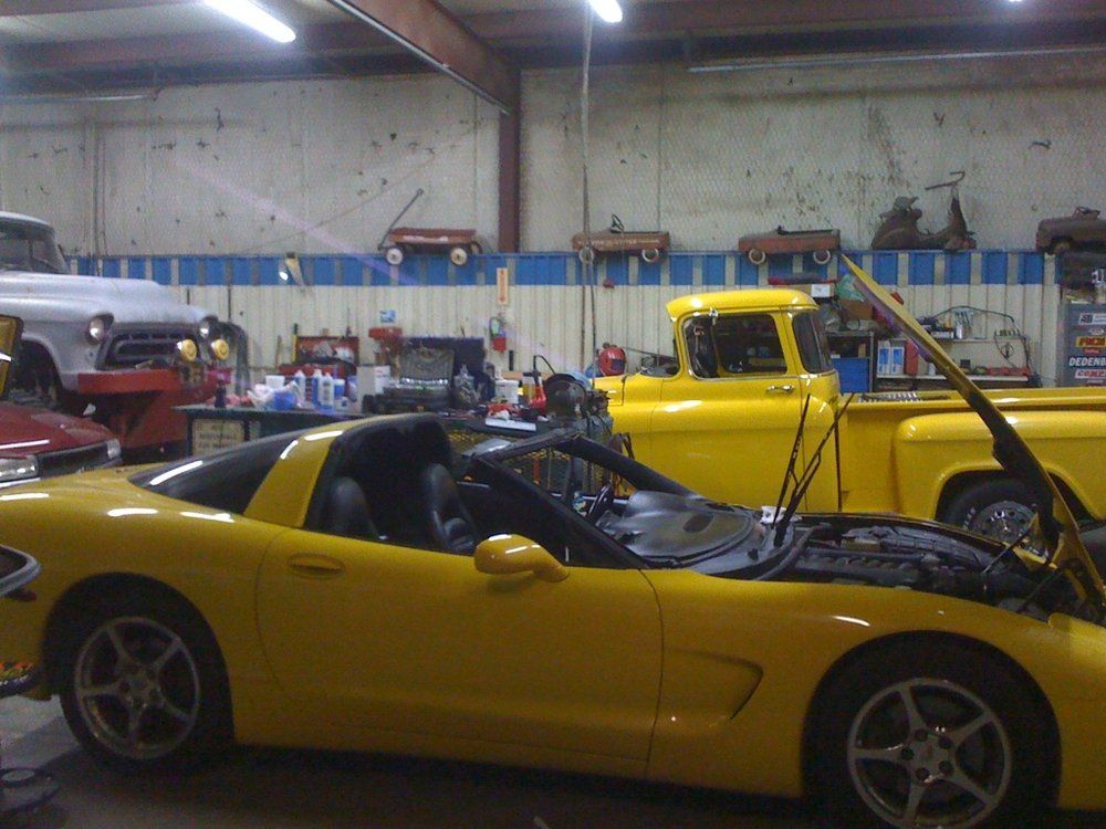 A yellow sports car is parked in a garage with its hood up.