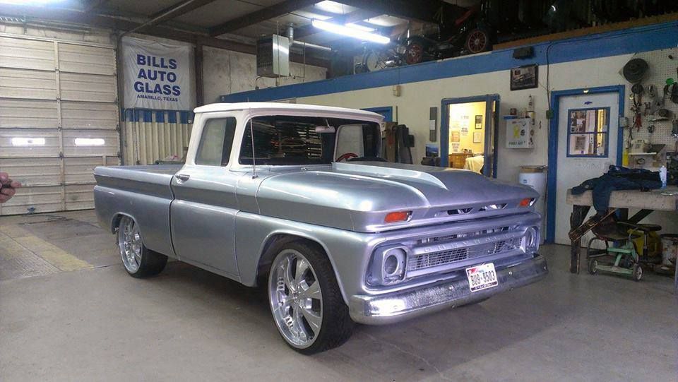A silver truck is parked in a garage next to a sign that says hills auto glass.