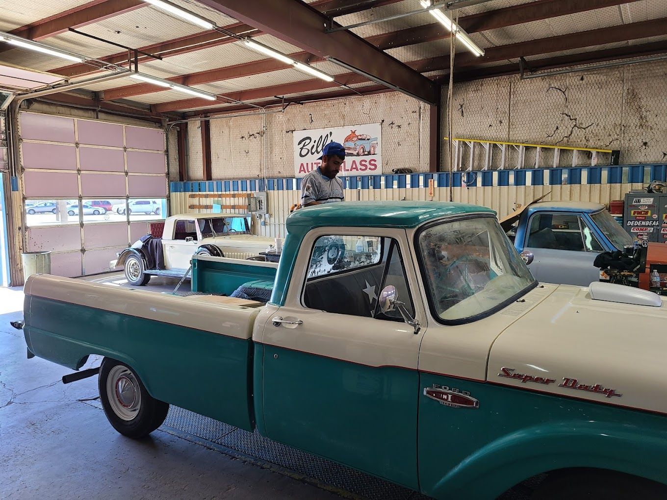A man is sitting on top of a blue and white truck in a garage.