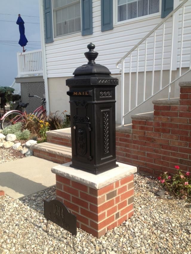 A black mailbox sits on a brick post in front of a house