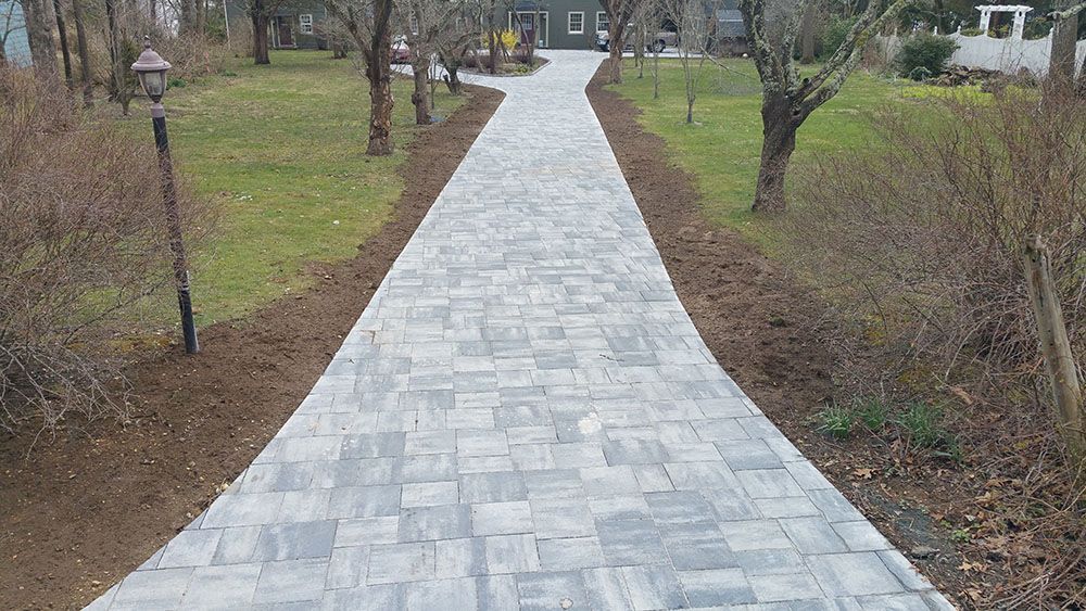 A brick driveway leading to a house surrounded by grass and trees