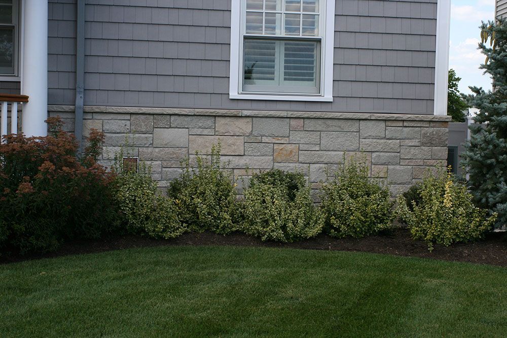 A house with a stone wall and a lawn in front of it
