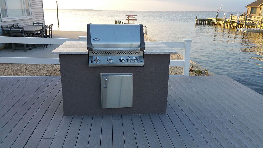 A grill is sitting on a wooden deck near the water