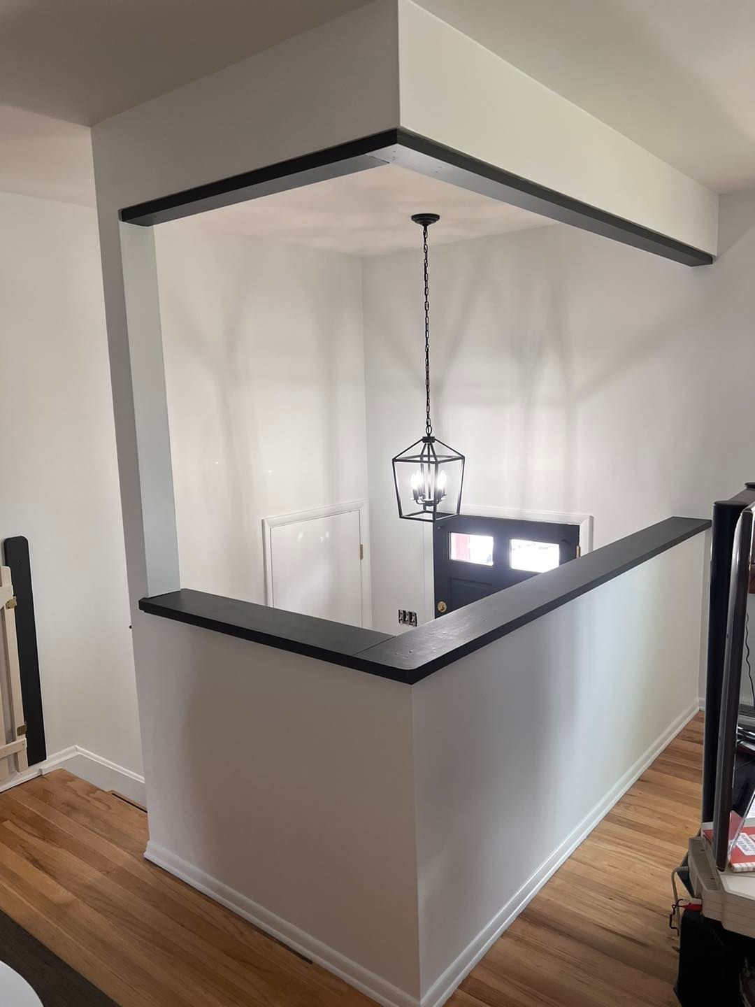 Interior view of a renovated entryway. White walls with black trim and a hanging lantern illuminate the dark front door.