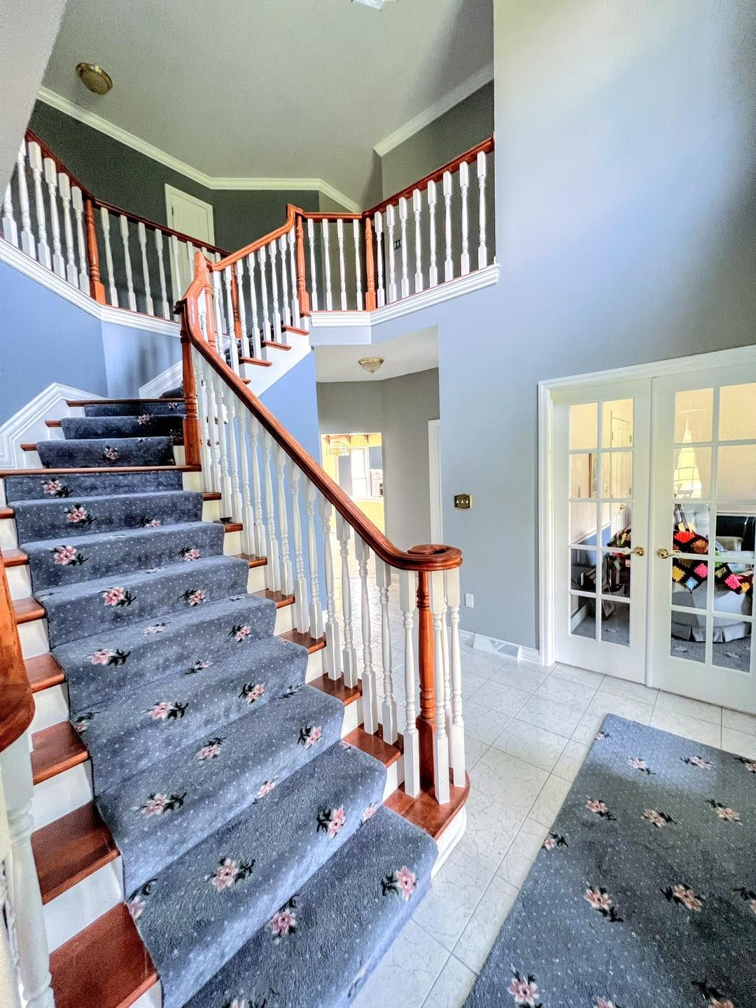 A grand foyer with a winding staircase and a blue and white color scheme. Double doors are on the right.